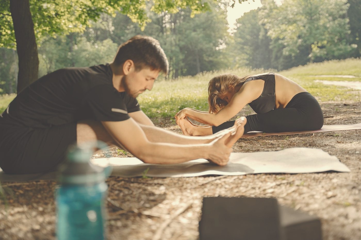 Two people stretching on yoga mats in warm park light.